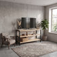 Mueble AArhus de pino natural y acero negro con televisor, cesta y decoración en una sala de pared gris.